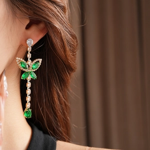 Close-up of butterfly and leaf earrings with green gems and crystals on a model