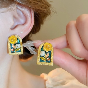 Macro detail of vintage gold floral earrings with green enamel and a white pearl inlay
