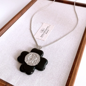 Close-up of black resin flower pendant with silver floral relief on a vintage chain