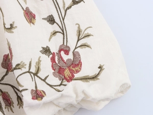 Detailed macro view of colorful floral embroidery and elastic pleated fabric on beige dress