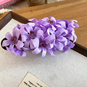 Macro shot of purple fabric flower hair clip with detailed petals on a wooden tray