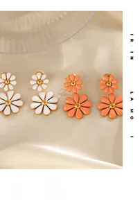 Detail of white and orange daisy drop earrings on champagne satin fabric background