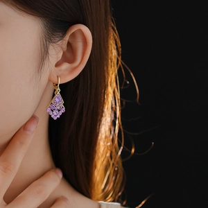 Detail of gold dangle earrings with purple stones on model in professional lighting