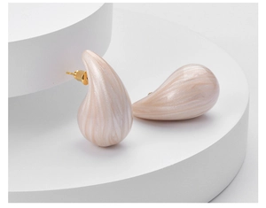 Detail of cream drop earrings with marble texture on geometric display stand
