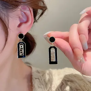 Detail of gold geometric earrings with black drip oil finish and CUTE rhinestone letters