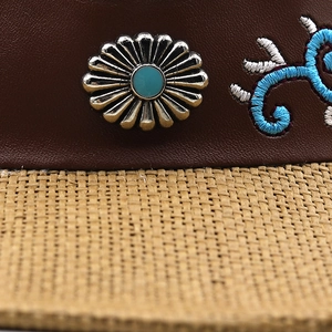 Close-up of leather band with turquoise stone inlay and floral embroidery on woven hat