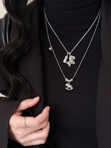 Detailed close-up of layered silver horse necklaces and beaded ring on black sweater