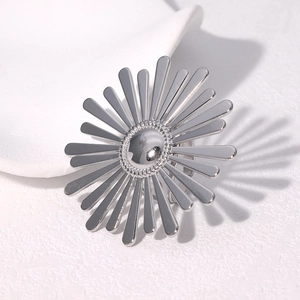 Silver sunflower metal brooch pin on textured white background with elegant long shadows