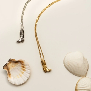 Silver and gold cowboy boot pendant necklaces displayed with decorative seashells