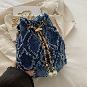 Blue denim bucket bag with fringe trim and pearl chain on a beige blazer background