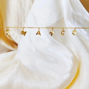 Detalle de collar de cadena cubana dorada con colgantes de letras EMANCO grabadas