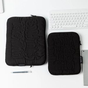 Detail of black quilted laptop sleeve with Good Things Take Time embossed slogan