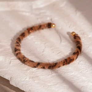 Macro view of leopard print faux fur open cuff with elegant gold ball ends on stone