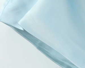 Detail of light blue satin fabric showing fine diagonal weave and silky texture on dress