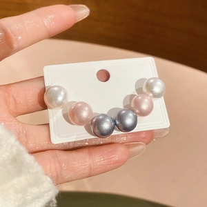 Detailed view of six iridescent faux pearls in white pink and grey on a display card