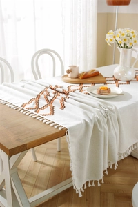 Close-up of geometric embroidery on beige tablecloth with elegant white tassels