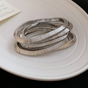 Macro detail of silver layered metal bracelet with ribbed texture on white ceramic tray