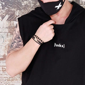 Close-up of men's leather punk bracelet with gold feather charm on a tattooed wrist
