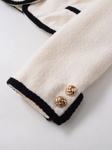 Détail du poignet d'une veste en tweed avec liseré noir et boutons dorés en blanc