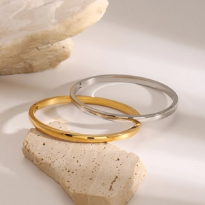 Detailansicht polierter Gold- und Silberarmbänder mit Scharnier auf einer beigen Steinplatte