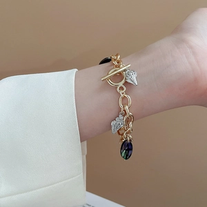 Detail of gold chain bracelet with silver seashell charms and purple gemstone on wrist