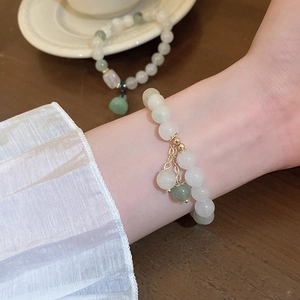 Close-up of white jade bead bracelet with green lotus seedpod charm and gold tassel