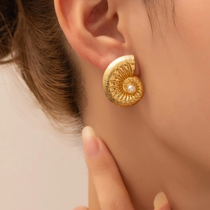 Close-up of golden spiral conch shell earring featuring a central white pearl inlay
