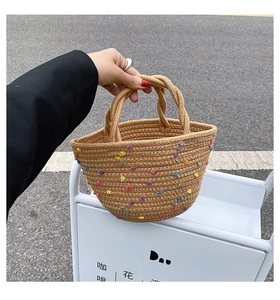 Detail of handmade straw bucket bag with colorful pom-poms and woven handles for summer