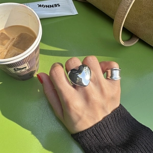 Polished heart ring and textured wide silver band worn together on a green desk