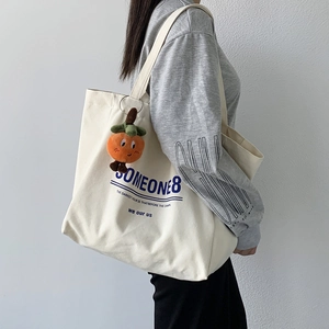Detail of a large off-white canvas shoulder bag with orange persimmon plush charm