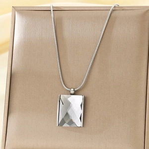 Macro view of silver snake chain necklace with clear rectangular crystal on gold jewelry box