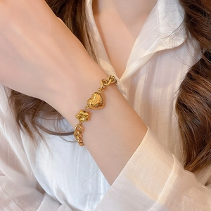 Detailed shot of a gold heart charm and textured sphere on a chunky Cuban link bracelet