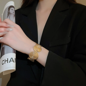 Close-up of golden spiral textured wide cuff bracelet worn with a black suit blazer