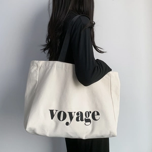 Large cream canvas tote bag with black voyage lettering and wide shoulder strap for travel