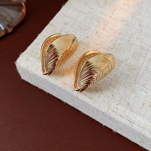 Macro shot of gold-colored textured shell earrings on a neutral linen background