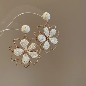 Detailed close-up of cream woven flower earrings with gold hollow frame and floral stud