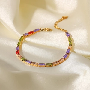 Détail d'un bracelet doré 18K avec zircons carrés multicolores sur un fond de soie