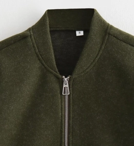 Detail of silver metal zipper and dark olive green fabric texture on bomber jacket