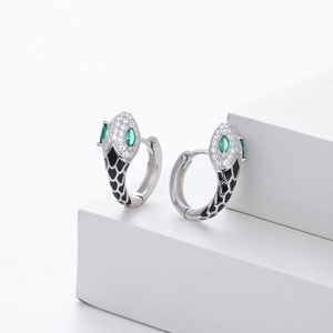 Macro detail of silver snake-shaped earring with green eyes and black scale patterns