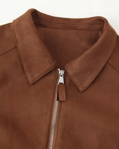 Détail du col d'une veste en daim marron avec fermeture éclair argentée et coutures