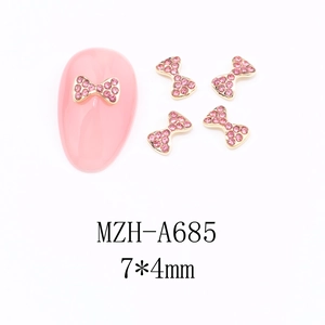 Macro detail of 7x4mm rose pink bow nail charms with gold base and rhinestones