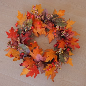 Close-up of artificial fall wreath with orange maple leaves and colorful berries on wood