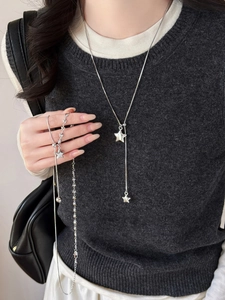 Detailed close-up of a silver asymmetric star necklace set on a dark grey knit sweater