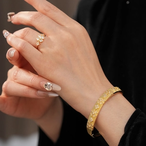 Detail of gold-plated flower ring and textured bangle set with zircon stones on a model
