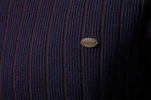 Detail of striped knitted sweater featuring high-quality vertical ribs and metal logo plate