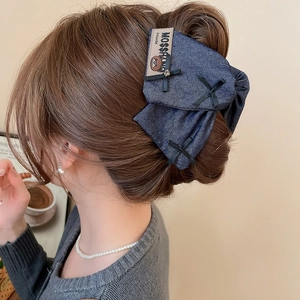 Detail of dark blue denim bow hair clip with silver rhinestones and embroidery on messy bun
