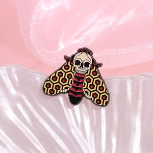 The Shining inspired moth enamel pin with geometric patterns on soft fabric background