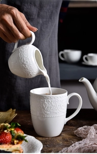Detail of pouring milk into a vintage embossed ceramic mug for afternoon tea