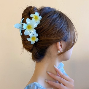 Detailed view of light blue and yellow frangipani flower hair claw on a woman's bun