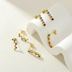 Macro shot of elegant curved gold earrings with colorful zircon stones on a white base